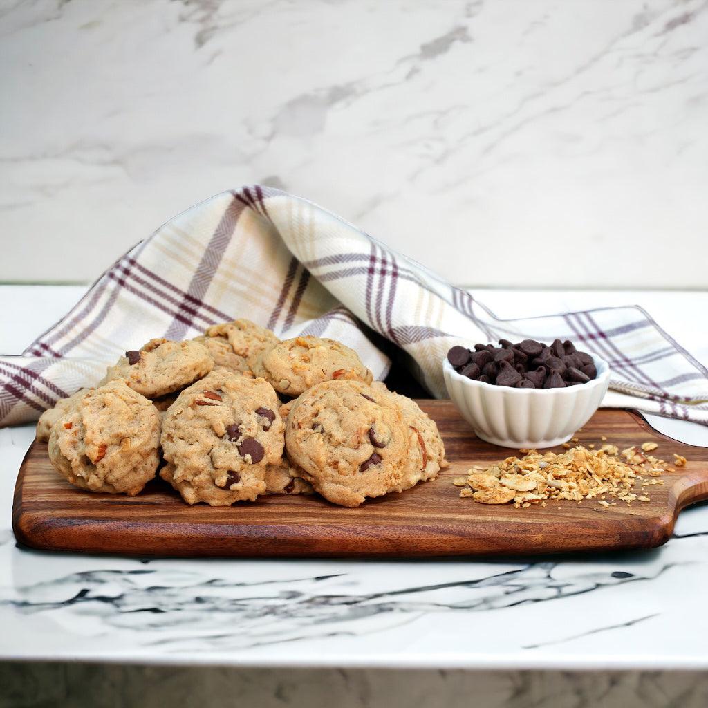 Pecan Chocolate Chip cookies on a wood block with a small bowl of chocolate chips and pecan scatter with a linen napkin on a marble countertop.