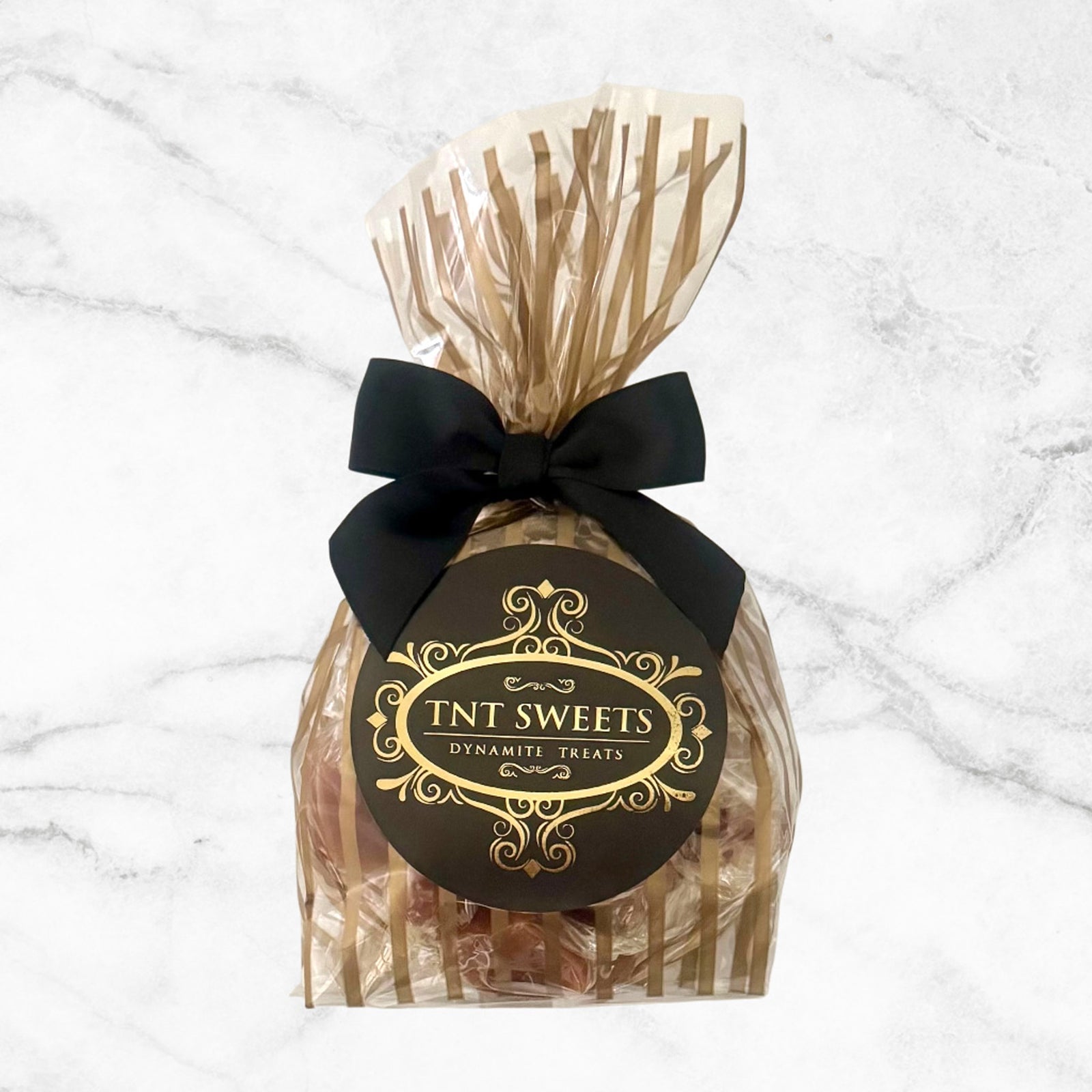 A half pound of caramels packaged in a gold striped cello bag with a black satin bow on a white marble background.