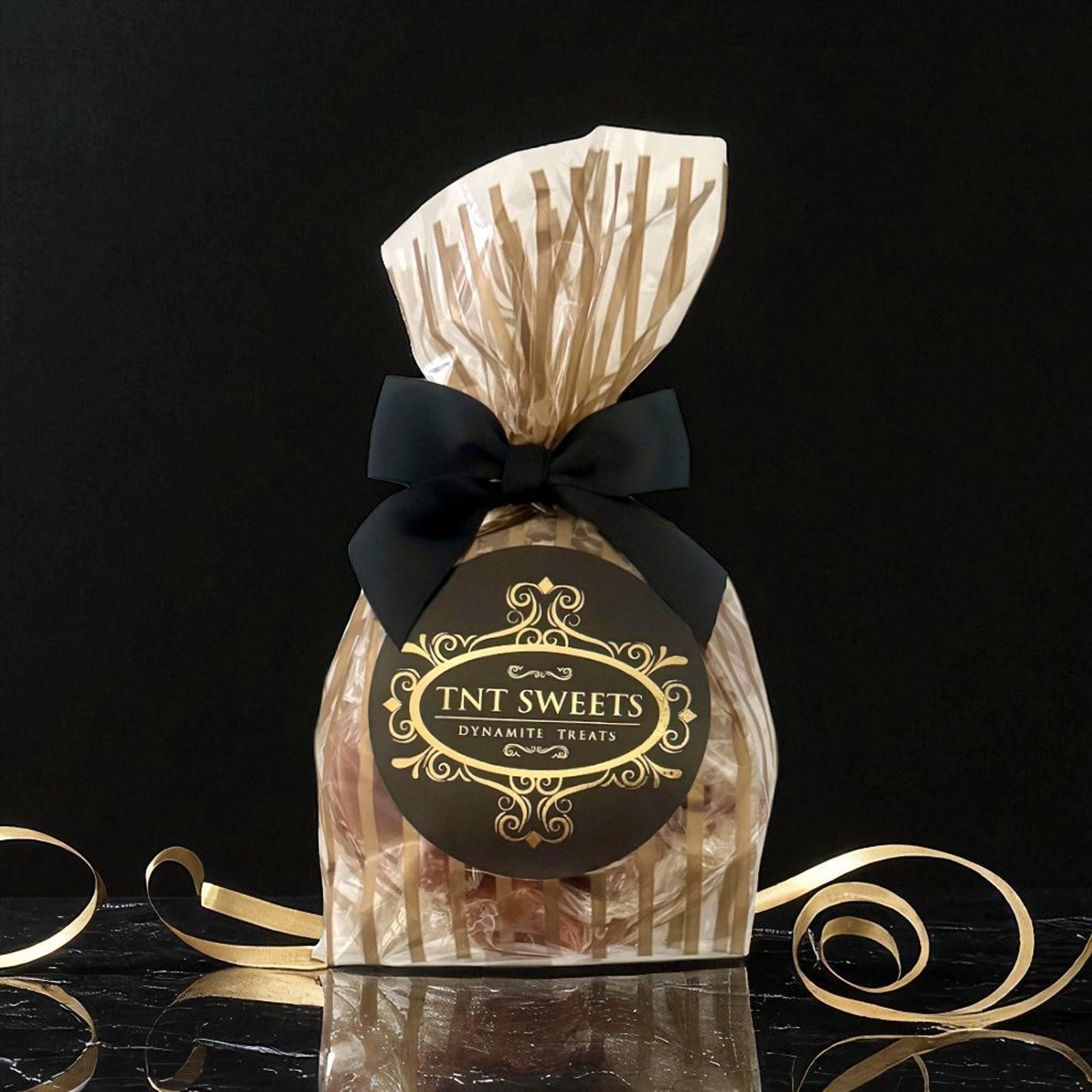 Gold striped gift bag of TNT Sweets treats with logo on a black background.