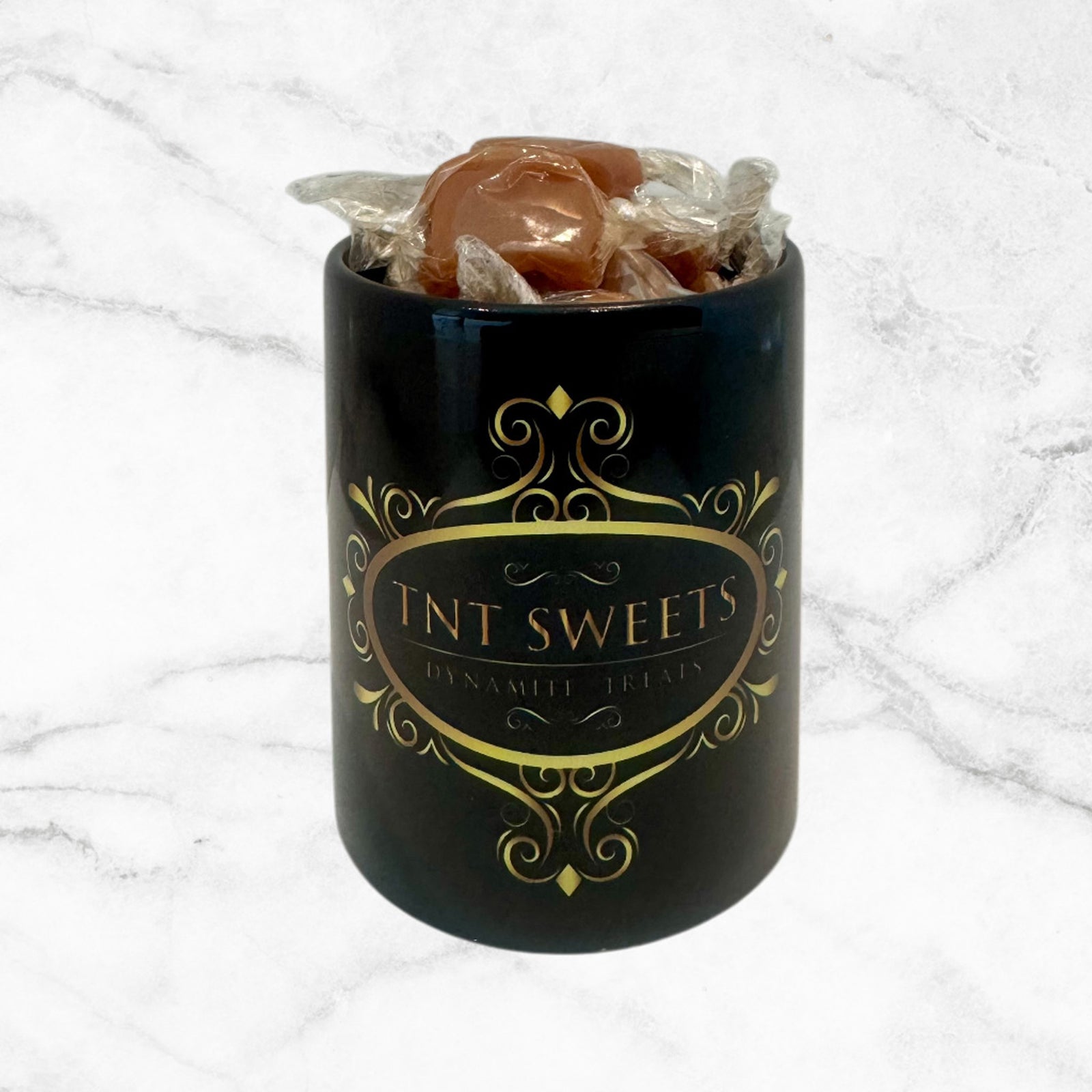 11oz TNT Signature black mug filled with caramels on a white marble background.