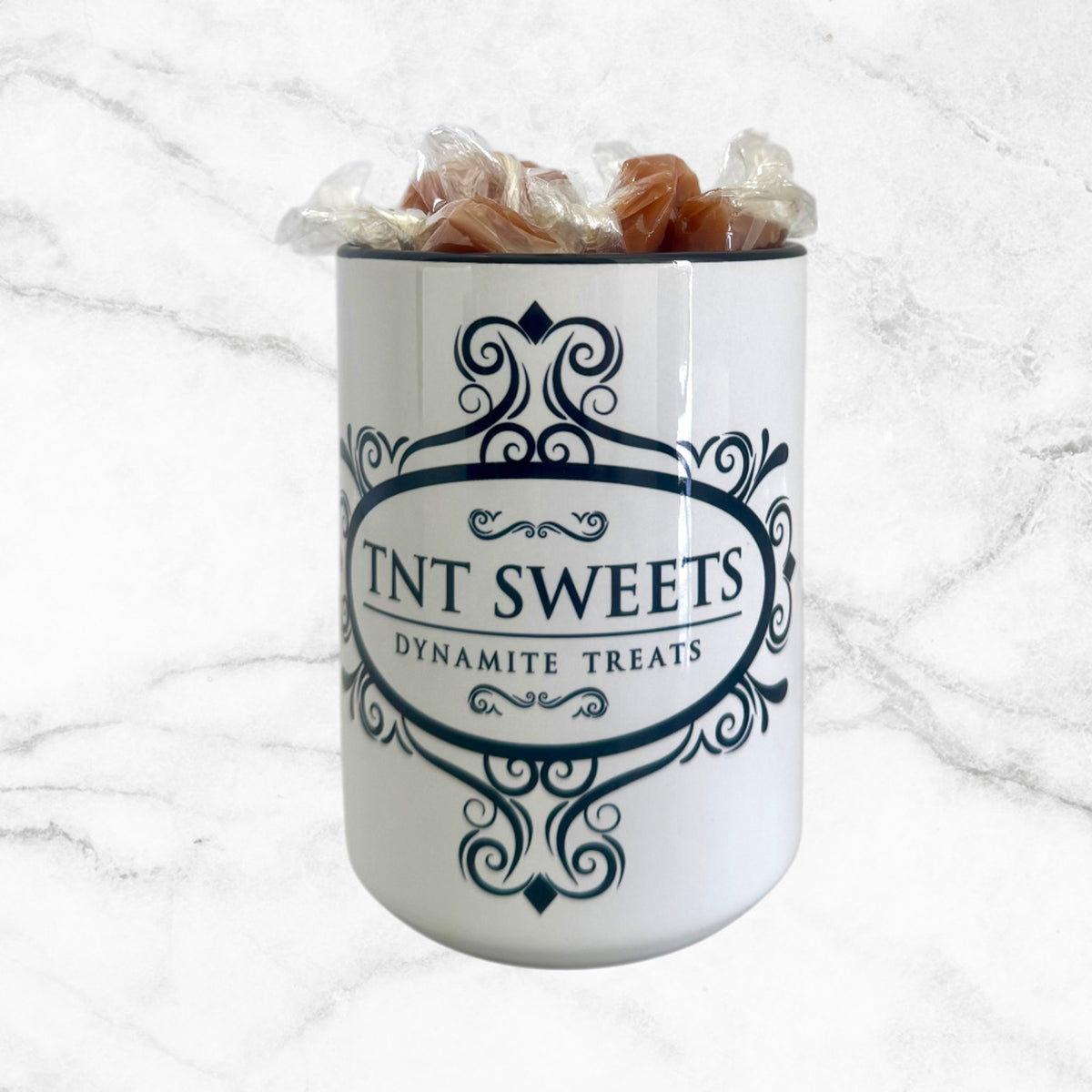 15oz TNT Signature White Mug filled with caramels on a white marble background.