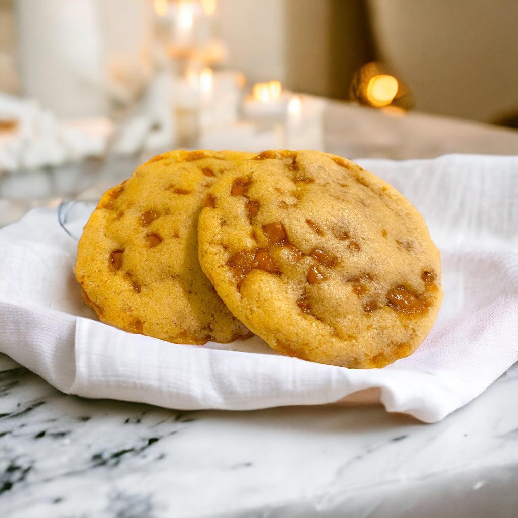 Two TNT toffee cookies on a linen napkin on a marble countertop with a blurred background.