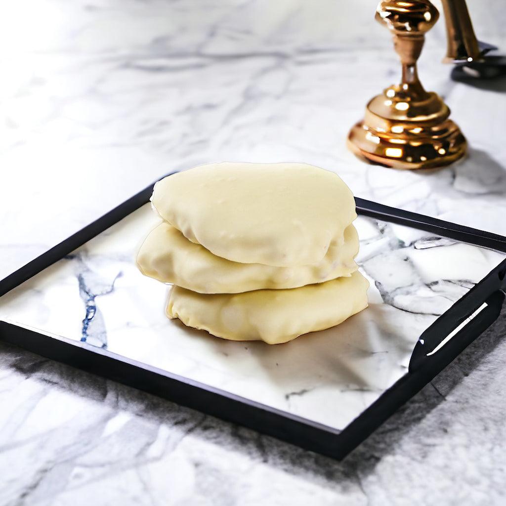 Stack of three white chocolate chews on a marble plate on a marble countertop.