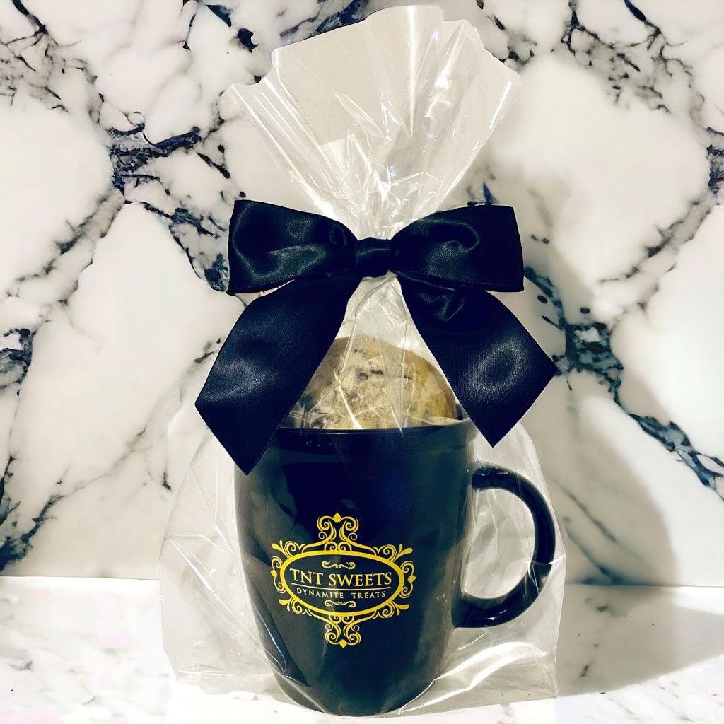 Chocolate Chip cookies filled in an 18oz mug wrapped in cellophane with a black bow on a marble countertop.
