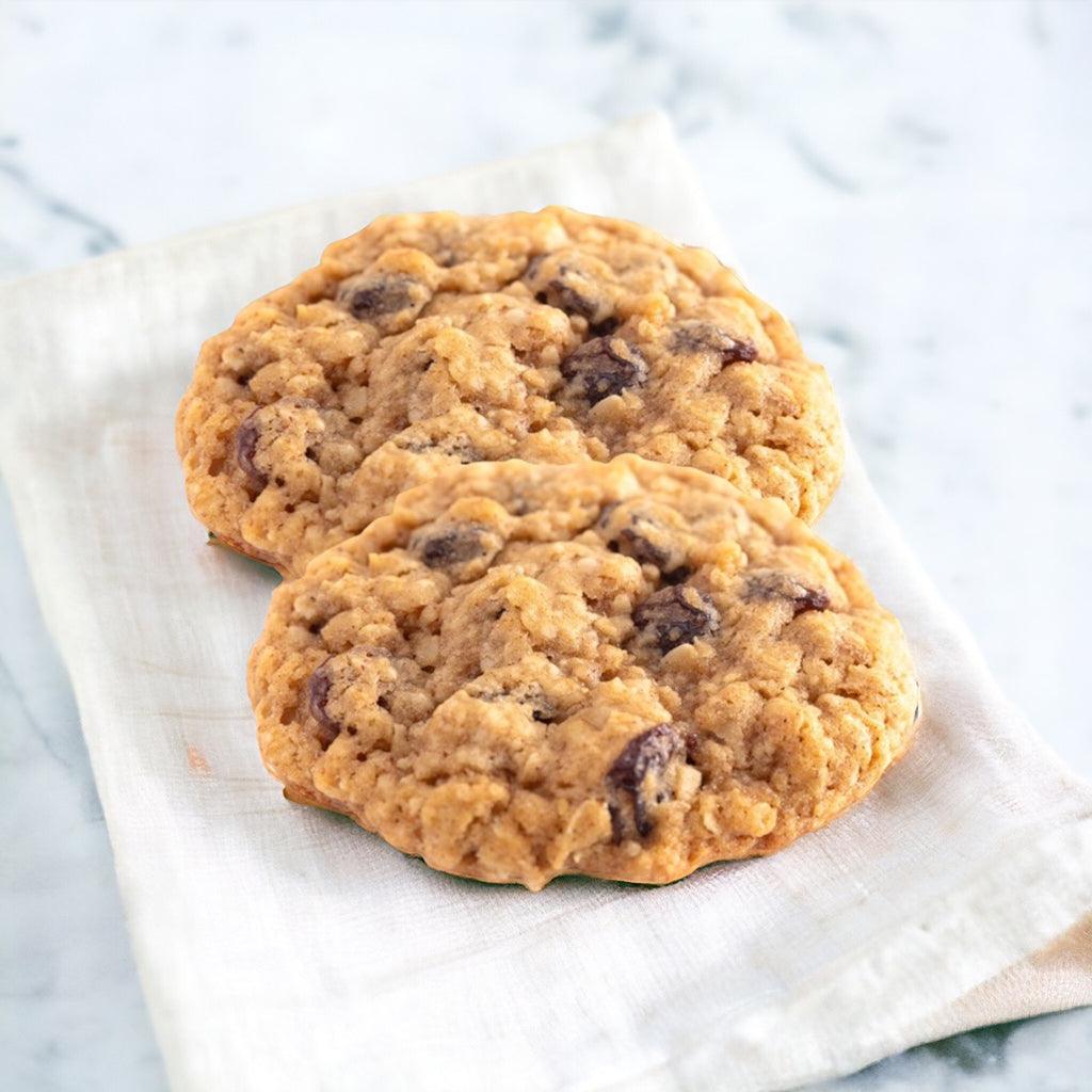 Two Oatmeal Raisin Cookies on a linen napkin with on a marble countertop.