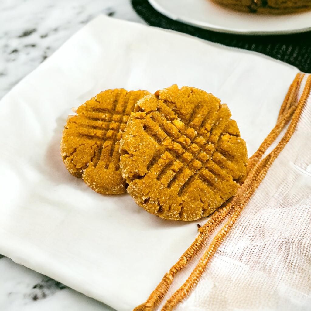 Two Peanut Butter Cookies on a linen napkin on a marble countertop.