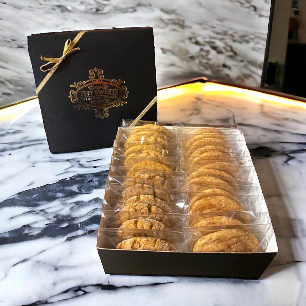An assortment of cookies in a TNT Sweets black signature cookie box on a marble table.