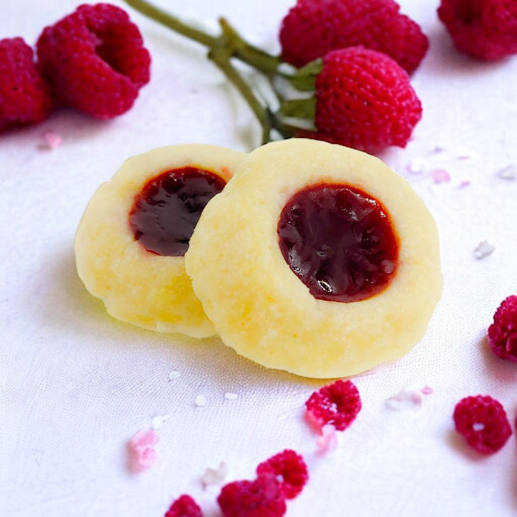 Two raspberry thumbprint cookies with scattered raspberries on a white tablecloth.