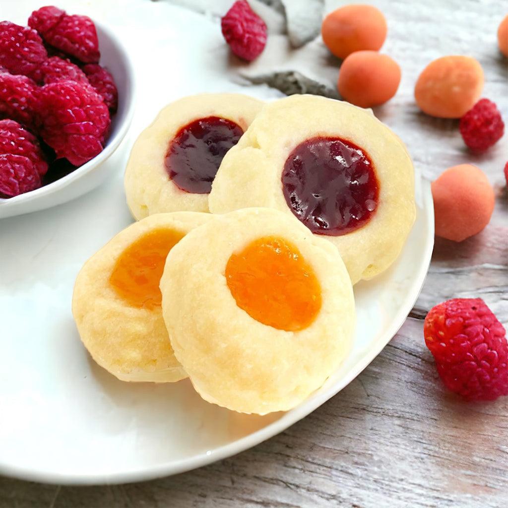 Apricot and raspberry thumbprint cookies on a plate with a bowl of fresh raspberries on a wooden countertop.