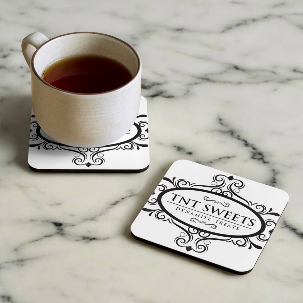 Two classic white TNT coasters with a black logo on a marble countertop with a cup of coffee sitting on one coaster.