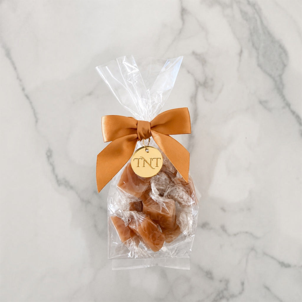 The Accent caramel favor by TNT Sweets with individually wrapped Amber Velvet sea salt caramels, gold satin ribbon, and gold TNT medallion.