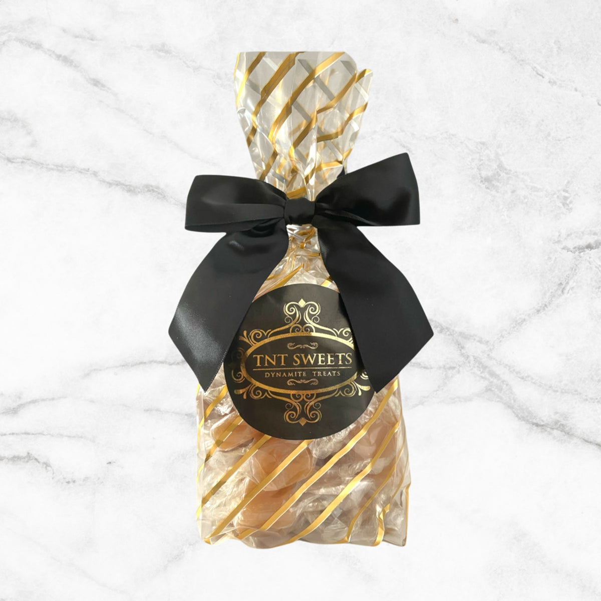 TNT Sweets one-pound Amber Velvet caramels in the Gold Stripe Wrap with black satin bow and TNT signature seal om a white marble background.
