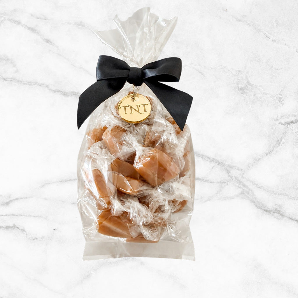 Clear half-pound bag of Amber Velvet sea salt caramels, finished with a black satin bow and gold TNT medallion.