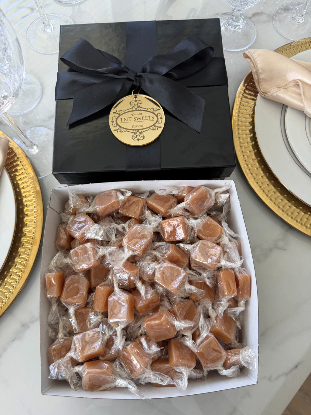 Two pounds of Amber Velvet Sea Salt Caramels from TNT Sweets in the black Keepsake Box tied with a black satin ribbon and finished with a gold acrylic medallion.
