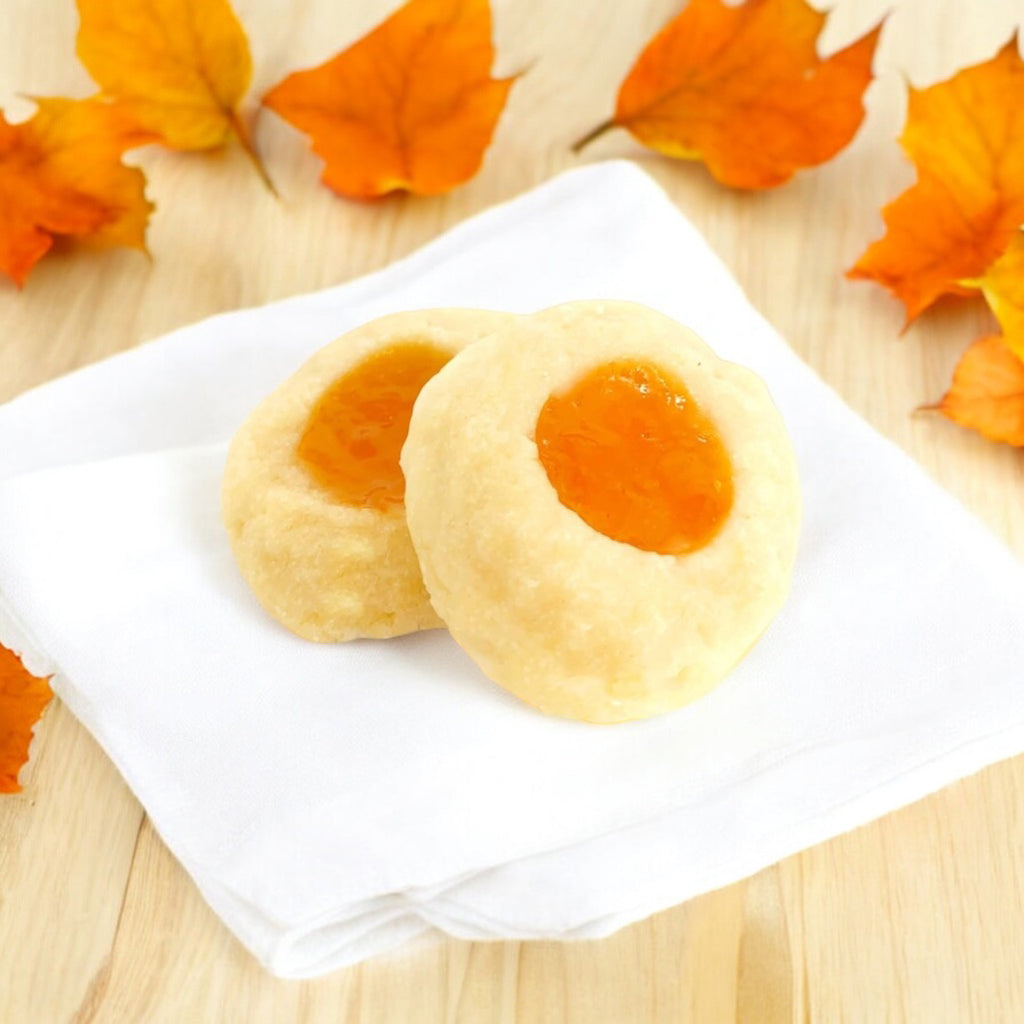 Two Apricot Thumbprint cookies on a linen napkin with scattered fall leaves.