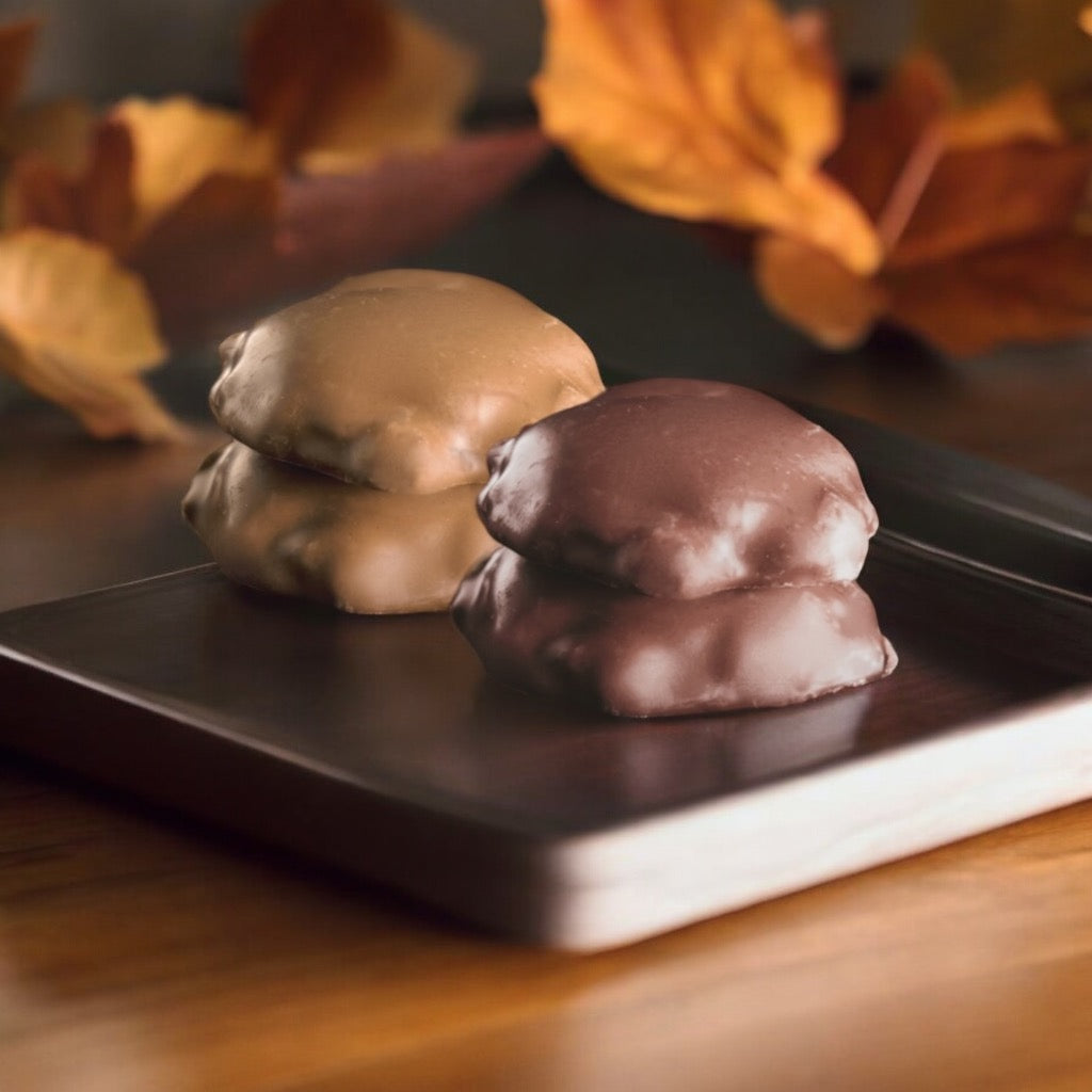 Milk chocolate and dark chocolate turtles on a tray on a wood countertop with fall leaves in the background.