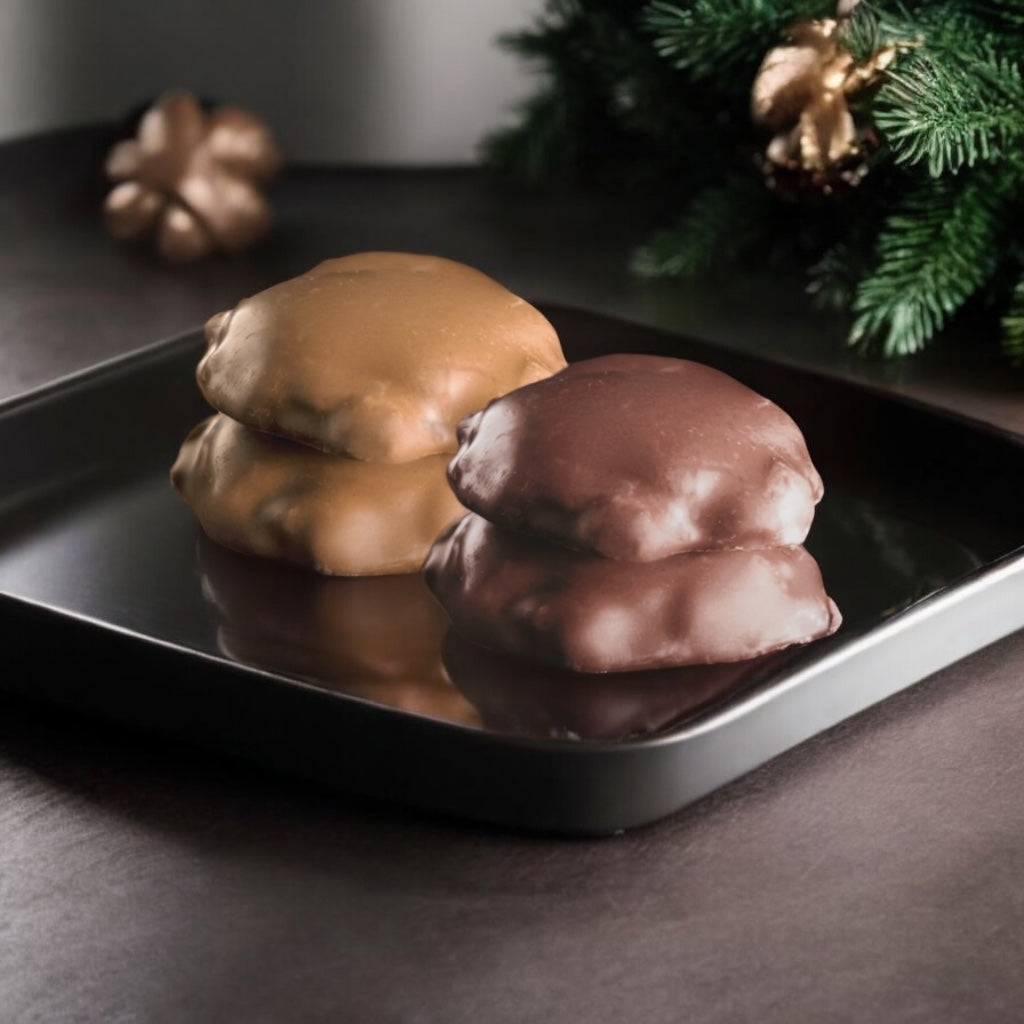 Milk chocolate and dark chocolate turtles on a tray on a wood countertop with pine leaves in the background.