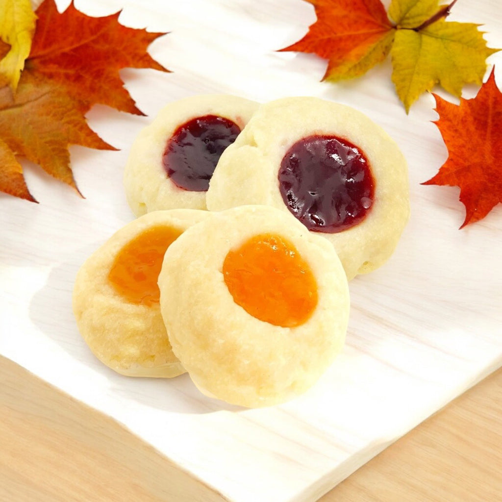 Two Assorted Thumbprint cookies on a linen napkin with scattered fall leaves.