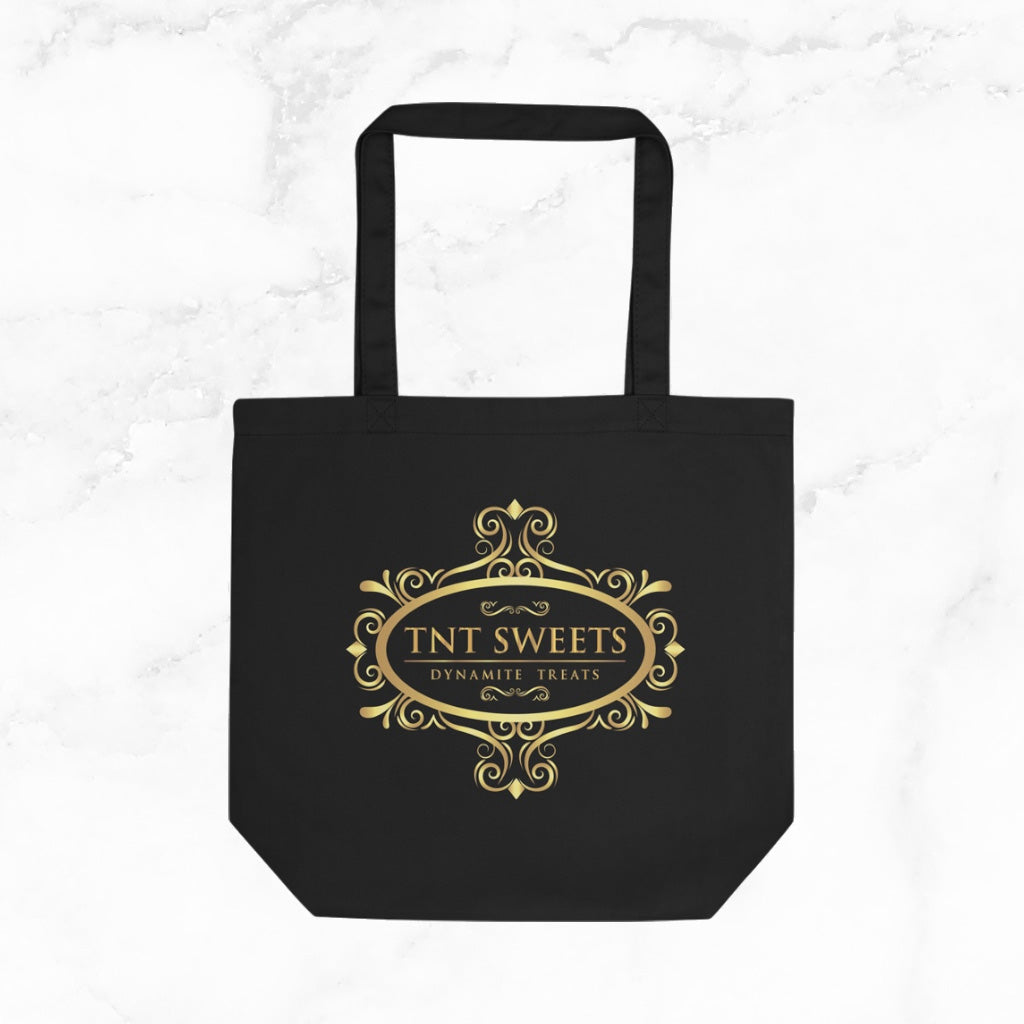 Black tote bag with gold TNT Sweets logo on a marble background.