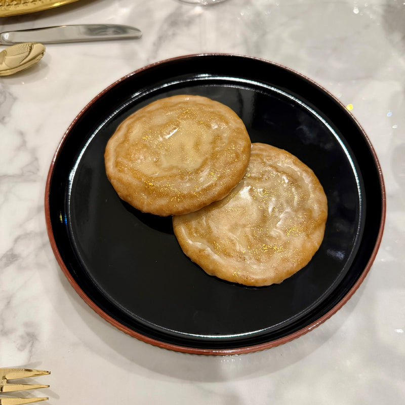 Two glazed Apple Calvados Cookie with 24-karat gold accents served on a black plate atop a white marble table.