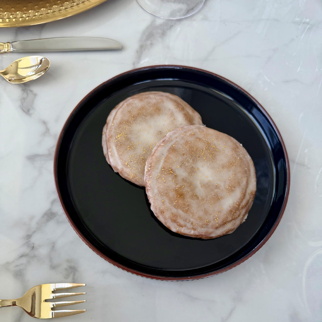Two glazed Apple Calvados with 24-karat gold accents served on a black plate atop a white marble table.