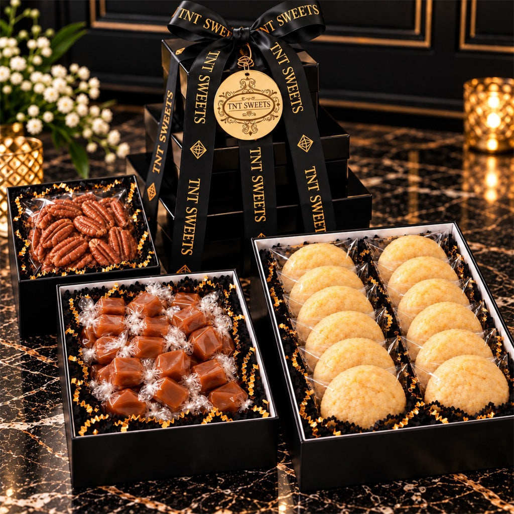 Black Tie Tower on dark marble, shown with its three keepsake boxes open: a dozen individually wrapped cookies, twist-wrapped caramels, and a bag of pecan halves in black-and-gold shred.