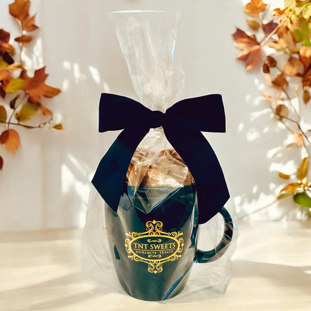 Candy filled in an 18oz mug wrapped in cellophane with a black bow on a wooden countertop with fall decor in the background.