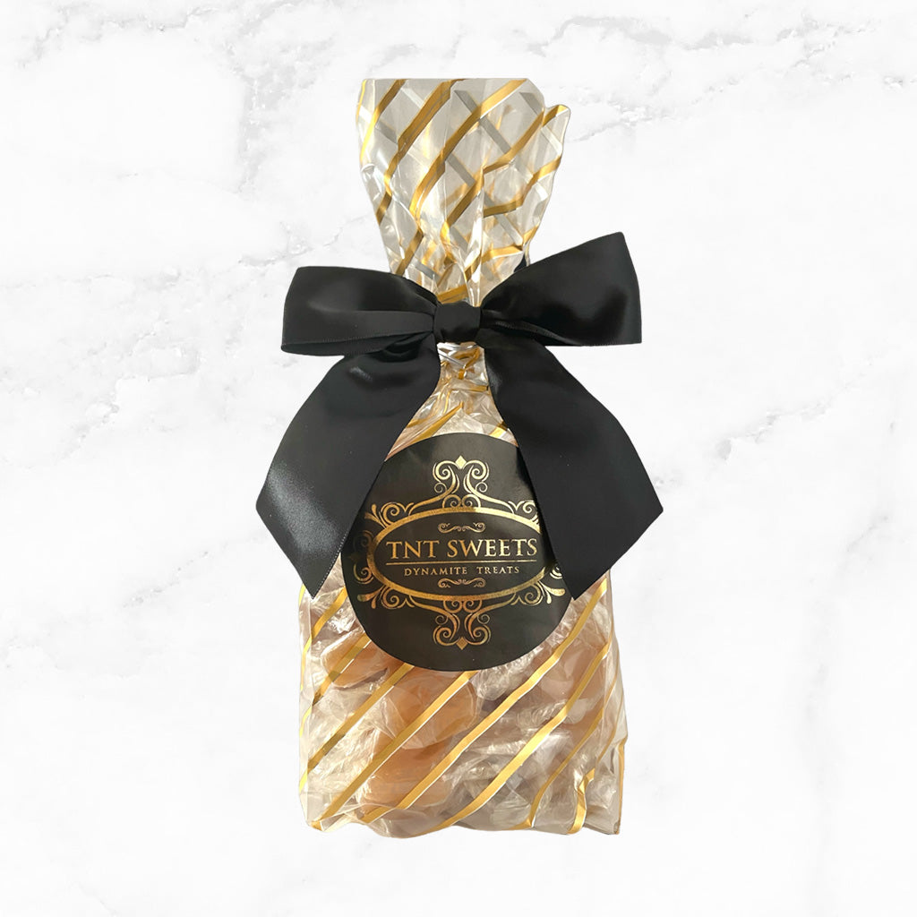 1lb caramels in a gold striped gift bag with a black bow on a white marble background.