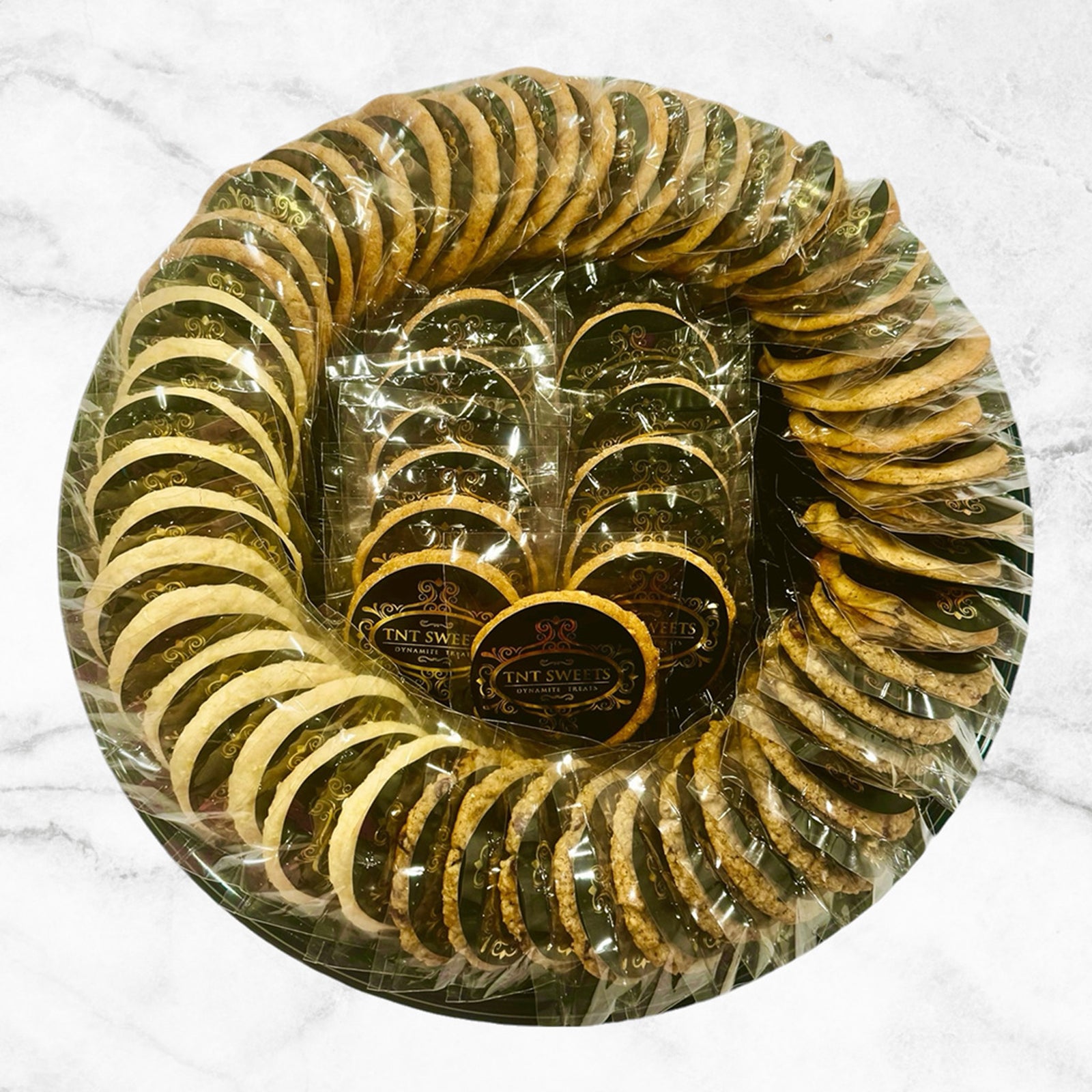 An assortment of five dozen cookies on a black cookie platter on a marble countertop.