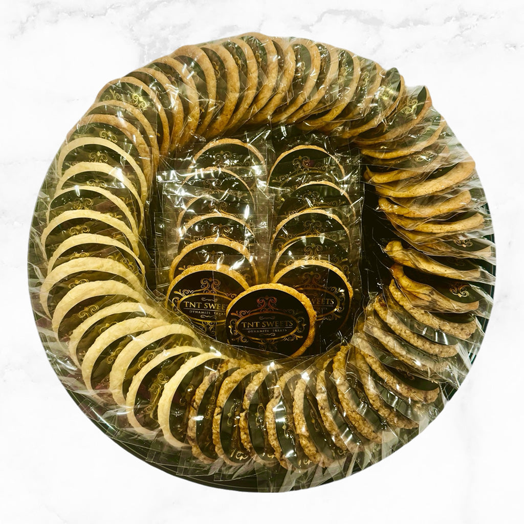 An assortment of five dozen cookies on a black cookie platter on a marble countertop.