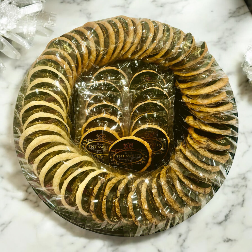 An assortment of five dozen cookies on a black cookie platter on a marble countertop with white decor in the background.