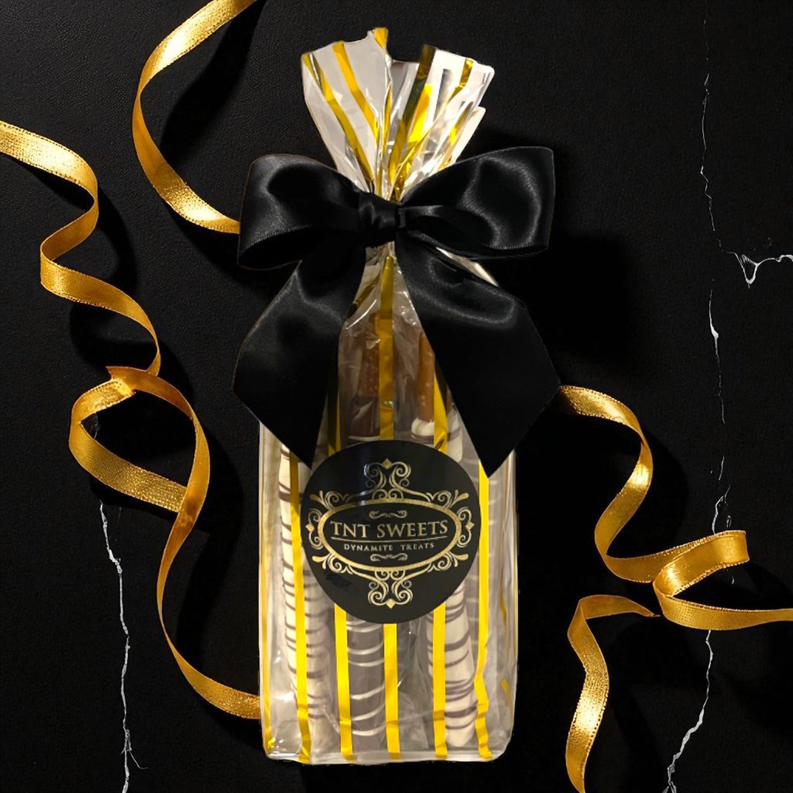 Gold striped gift bag of TNT Sweets with gold ribbons on a black background.