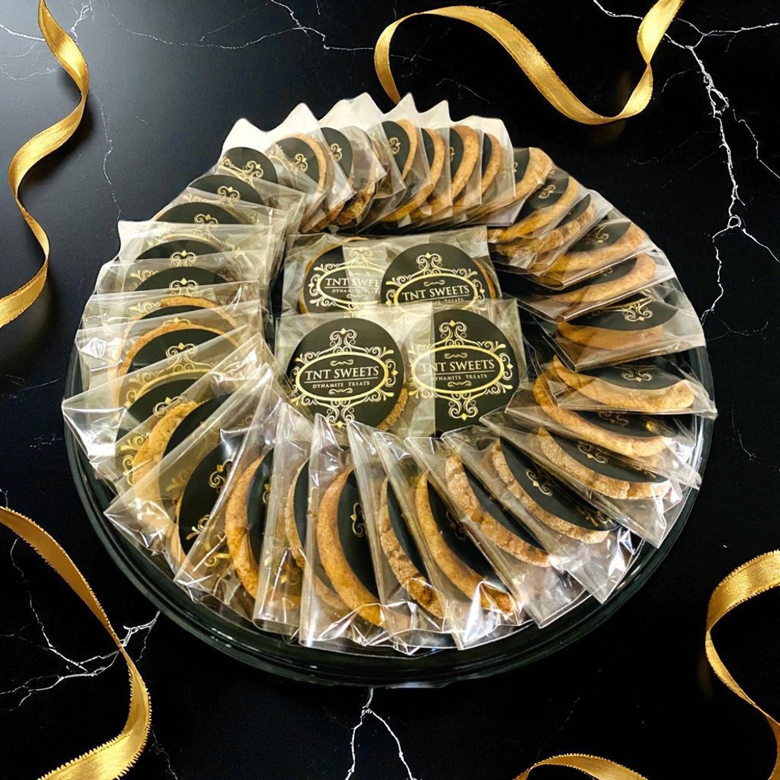 Three dozen cookies individually wrapped on a black platter on a white marble countertop.