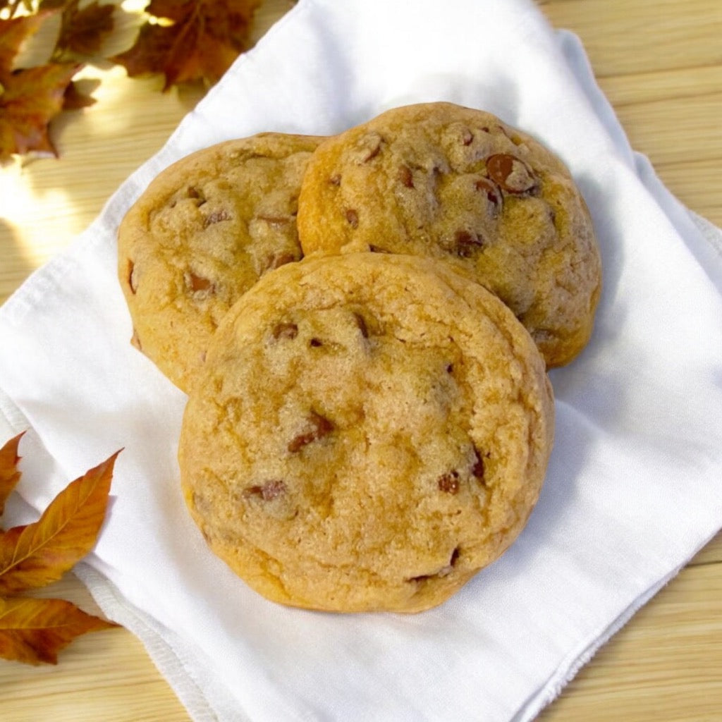 Three chocolate chip cookies on a linen napkin with scattered fall leaves