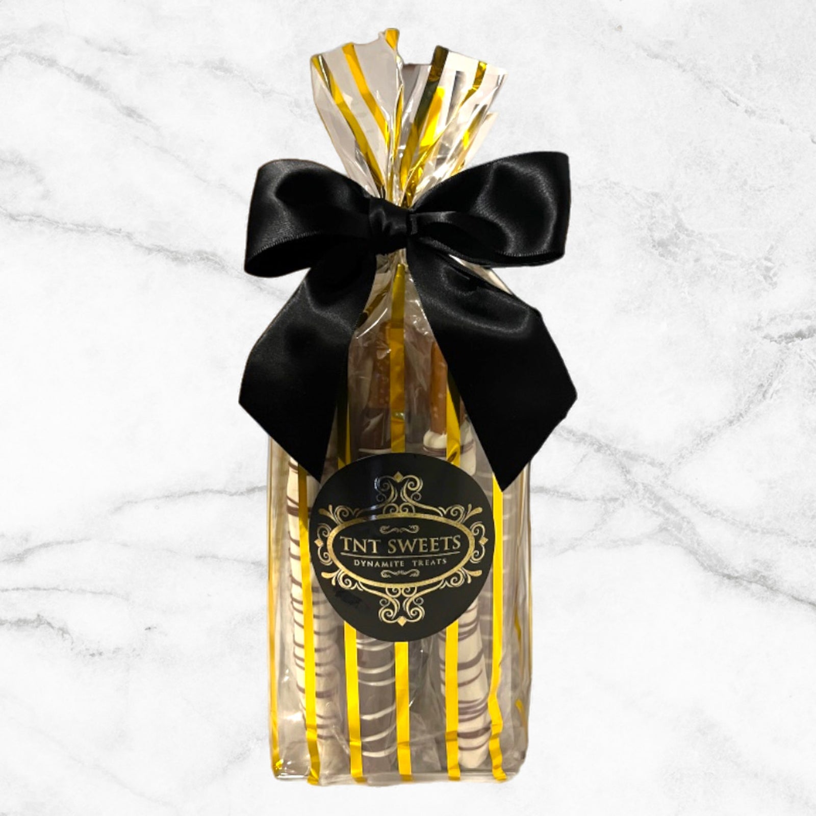 Pretzel medley in a gold striped gift bag with a black bow and label on a marble countertop.