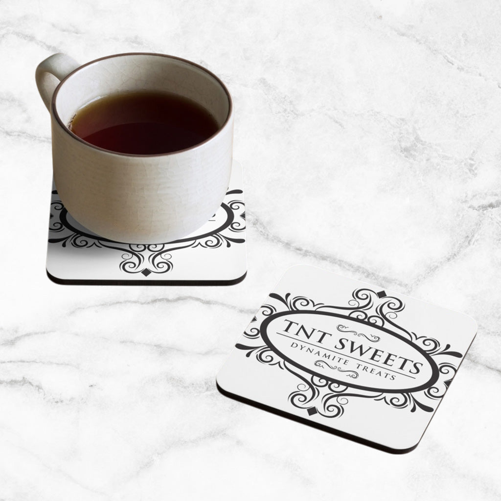 Two classic white TNT coasters with a black logo on a marble countertop with a cup of coffee sitting on one coaster.