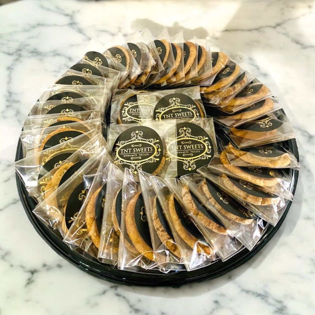 3 dozen cookies individually wrapped on a black platter on a white marble countertop.