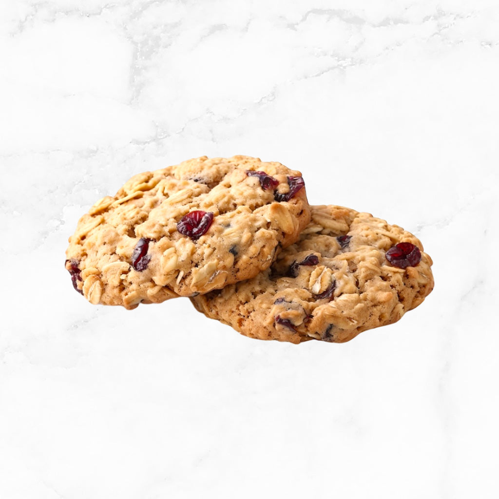 Two cranberry harvest cookies on a white marble countertop with scattered cranberries. 