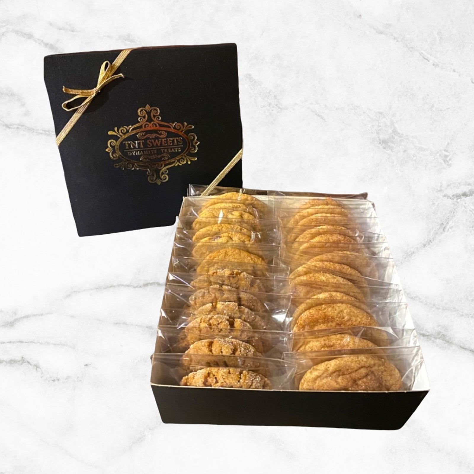 Two dozen cookies assorted in our signature black gift box with a gold ribbon on a white marble background.