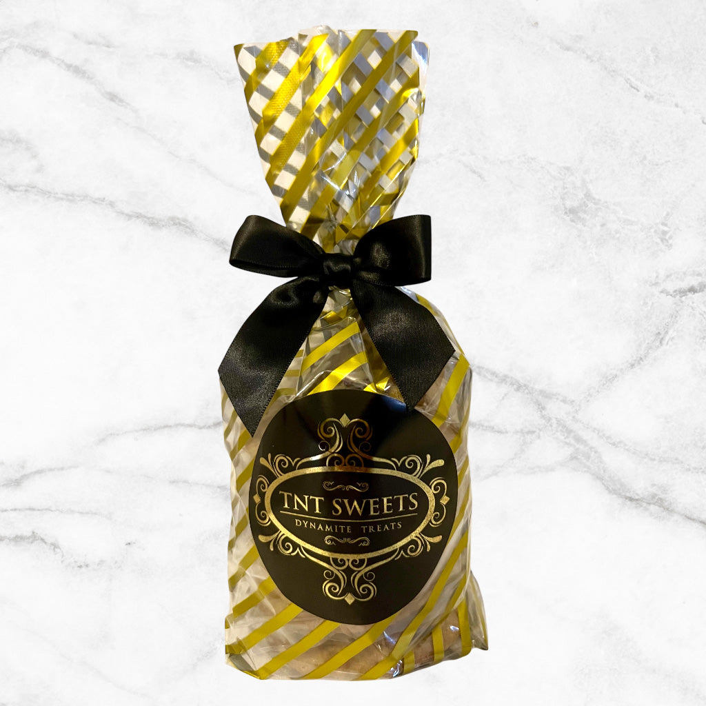Six cookies in a gold striped cello with a black and gold logo and tied with a black bow on a white marble background.