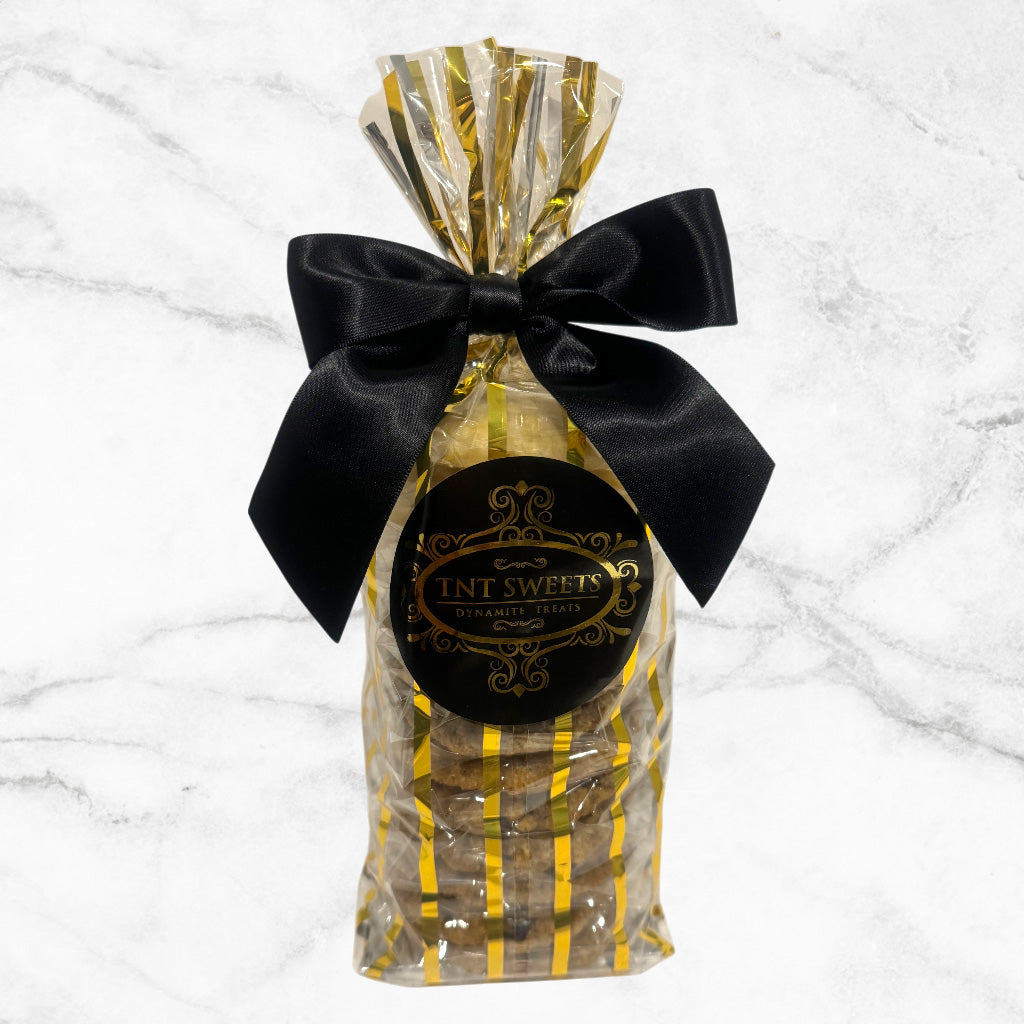 One dozen cookies assorted in a gold striped gift bag with a black bow on a marble background.