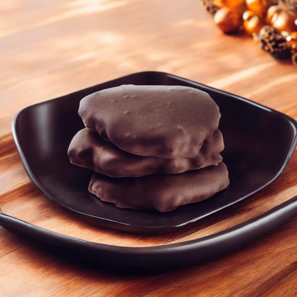 Stack of three Dark Chocolate chews on a brown plate on a wood countertop with fall decor in the background.