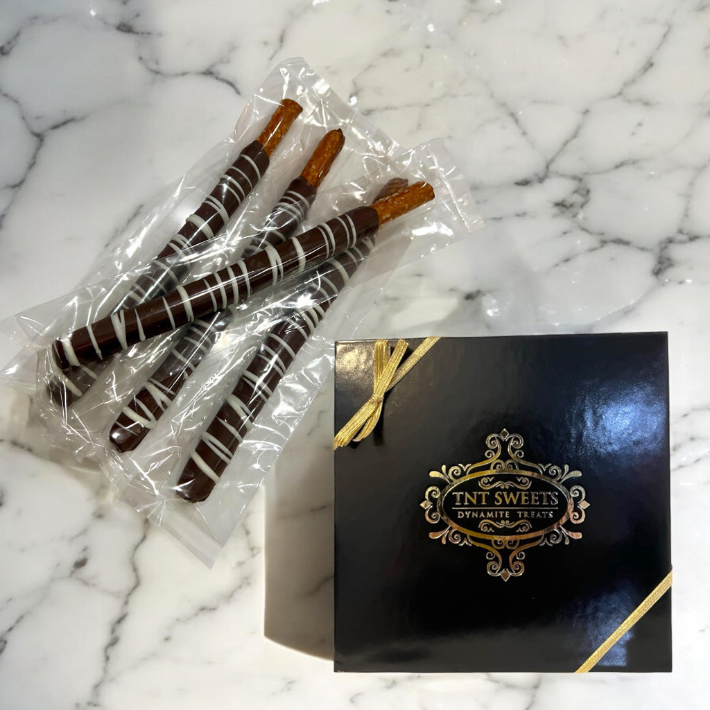 Chocolate-dipped pretzels in clear packaging on a marble countertop with a TNT Sweets black gift box.