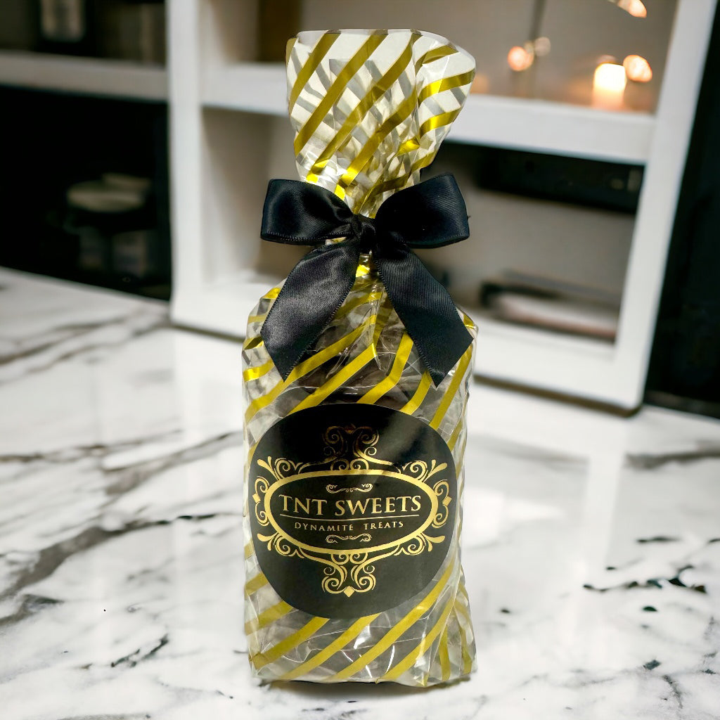 Dark chocolate turtles in a gold striped gift bag with a black bow on a marble countertop.