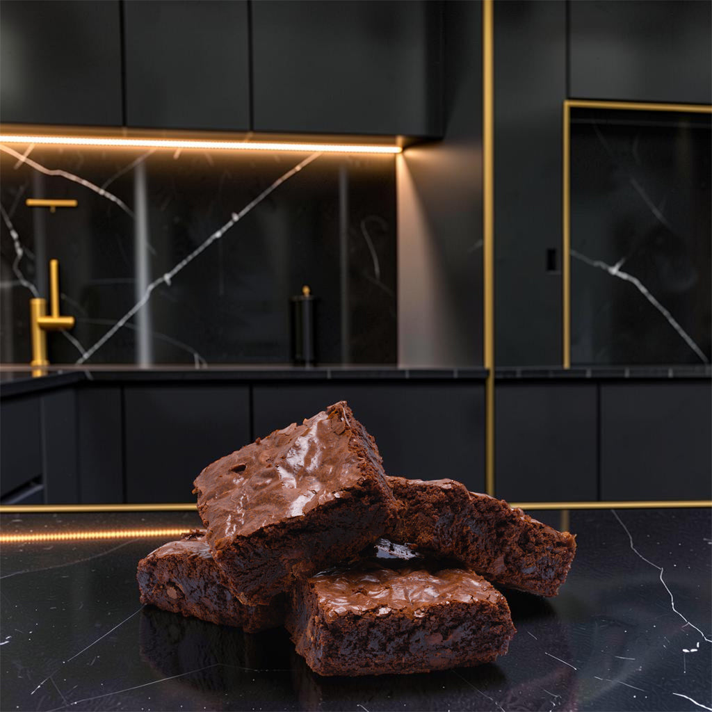 Four Dark Magic brownies from TNT Sweets made with Callebaut Belgian dark chococlate on a black marble countertop with a modern kitchen backdrop.
