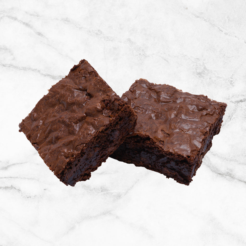Two Dark Magic gluten-free dark chocolate brownies from TNT Sweets made with Callebaut Belgian dark chocolate and premium European butter, displayed on a white marble surface.