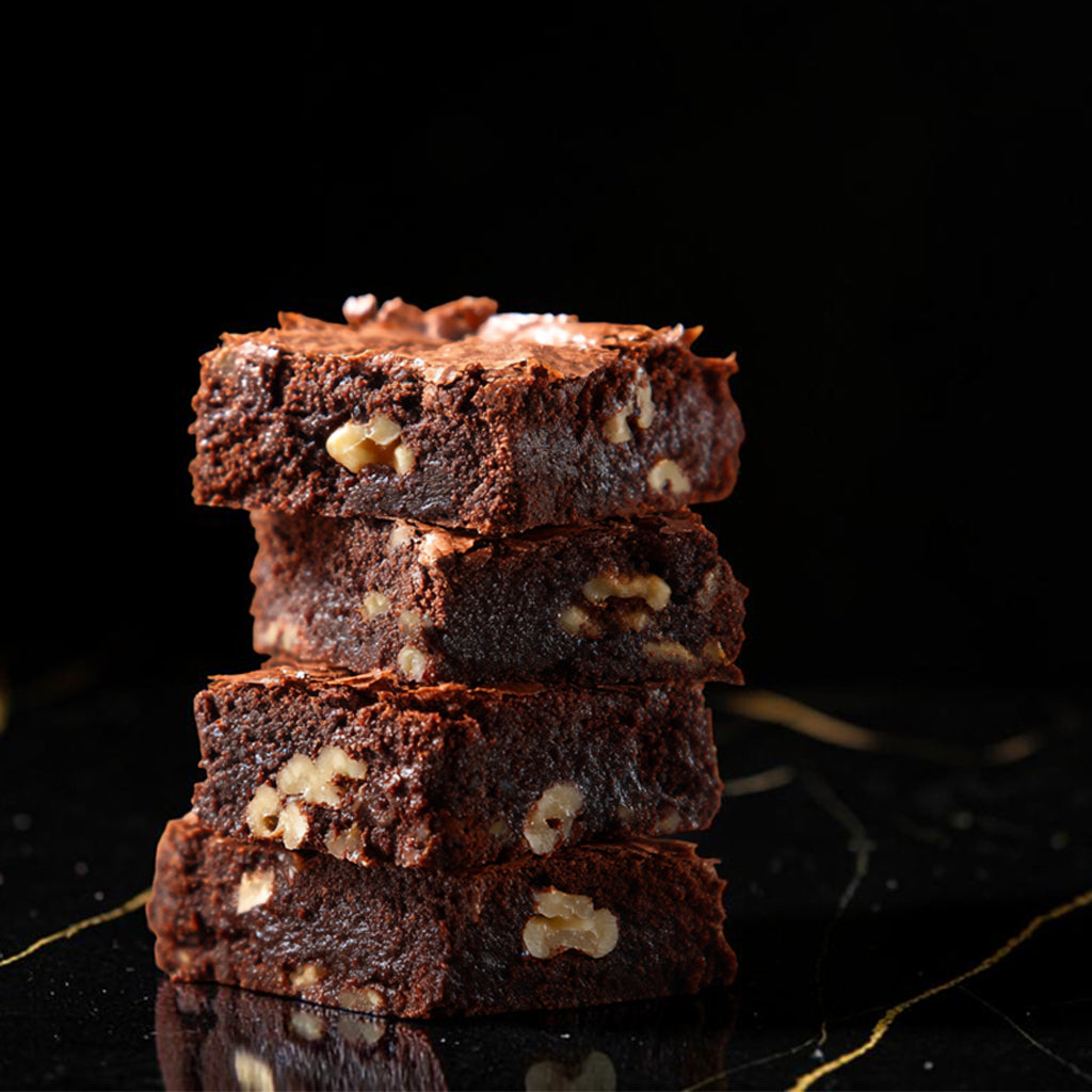 Stack of four Dark Magic pecan brownies from TNT Sweets featuring Callebaut Belgian dark chocolate and toasted San Saba Texas pecans on a black marble background. 