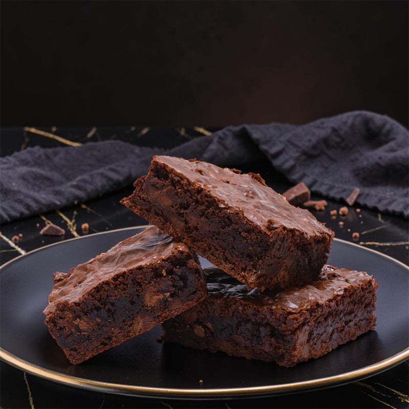 Three Dark Magic, dark chocolate brownies by TNT Sweets made with Callebaut Belgian Dark Chocolate and Madagascar vanilla on a black matte plate on a black marble surface.