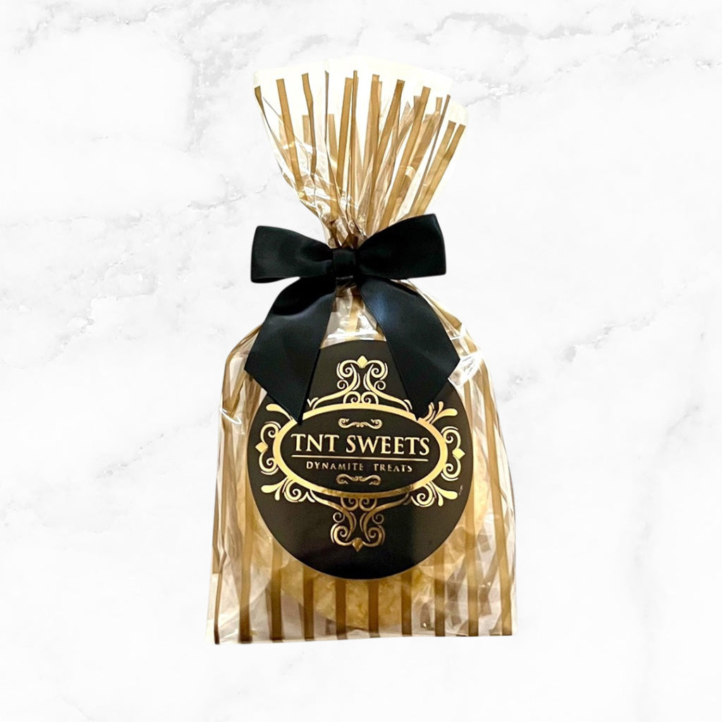 Two cookies in a gold striped bag tied with a black bow and black logo label with a marble background.