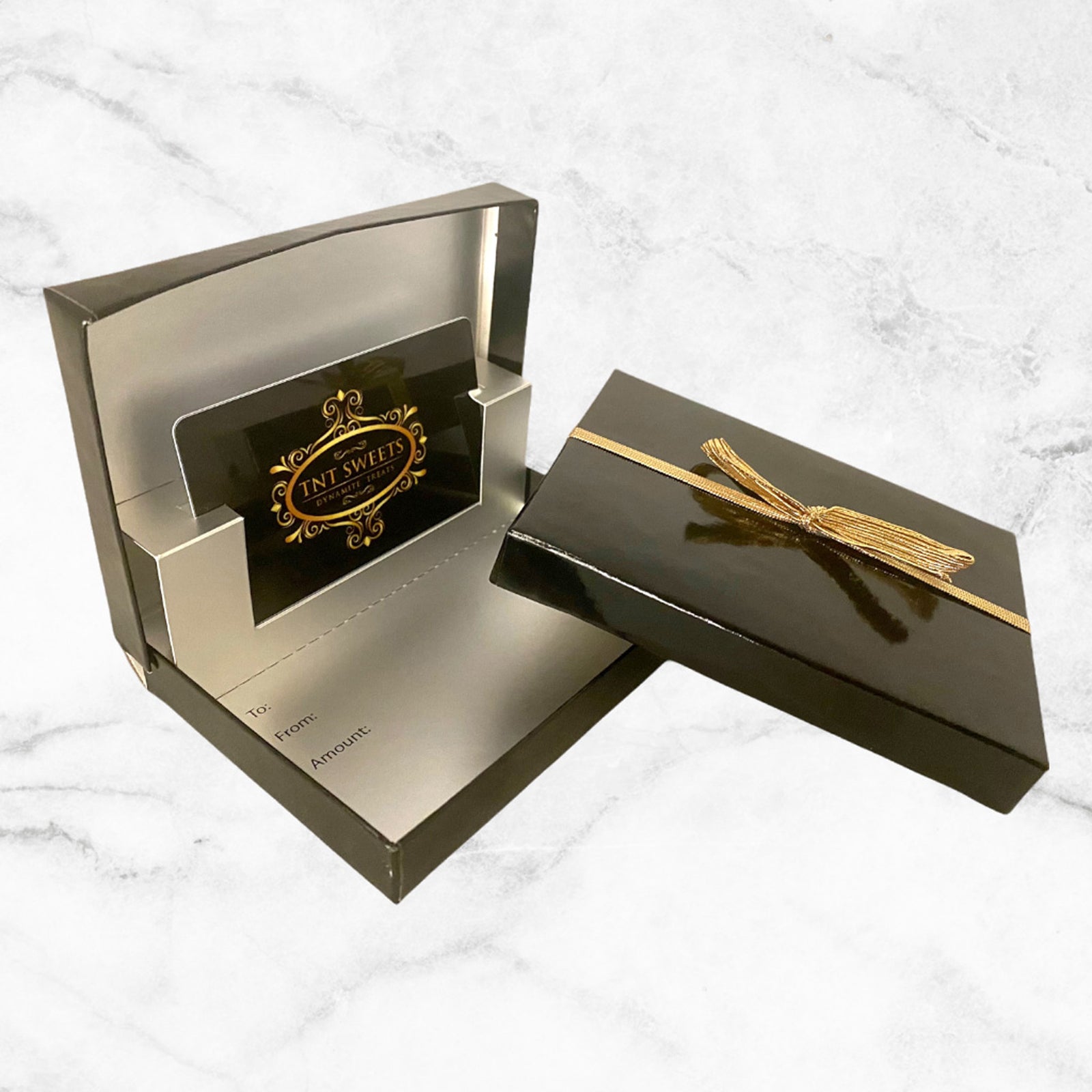TNT Sweets gift card box with gold bow showing gift card inside on a white marble background.